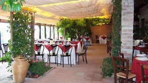 Un espace de restauration intérieur avec des tables dressées pour les clients, recouvert d’un auvent blanc et entouré de verdure.