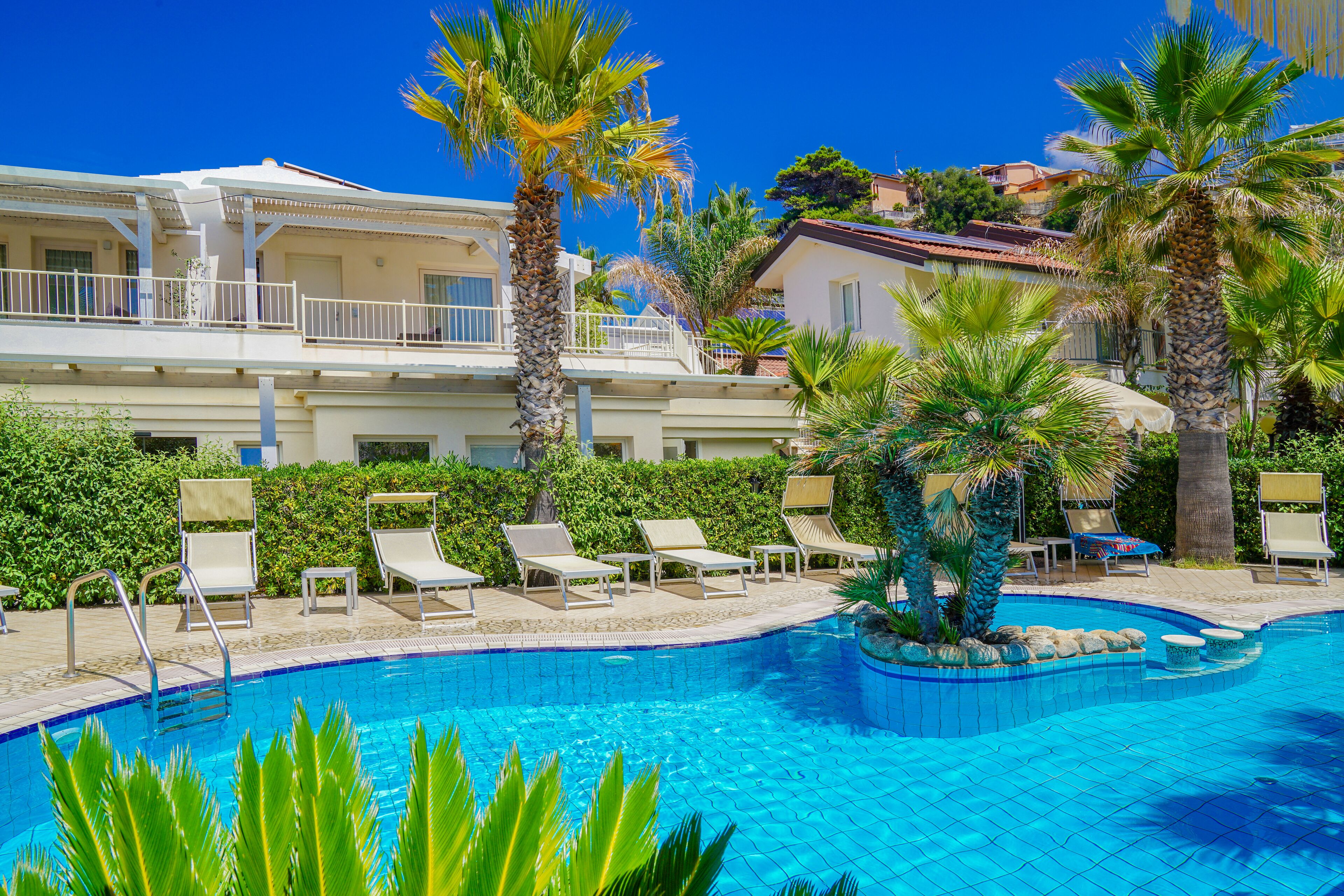 A swimming pool with lounge chairs and palm trees, surrounded by a building with balconies.