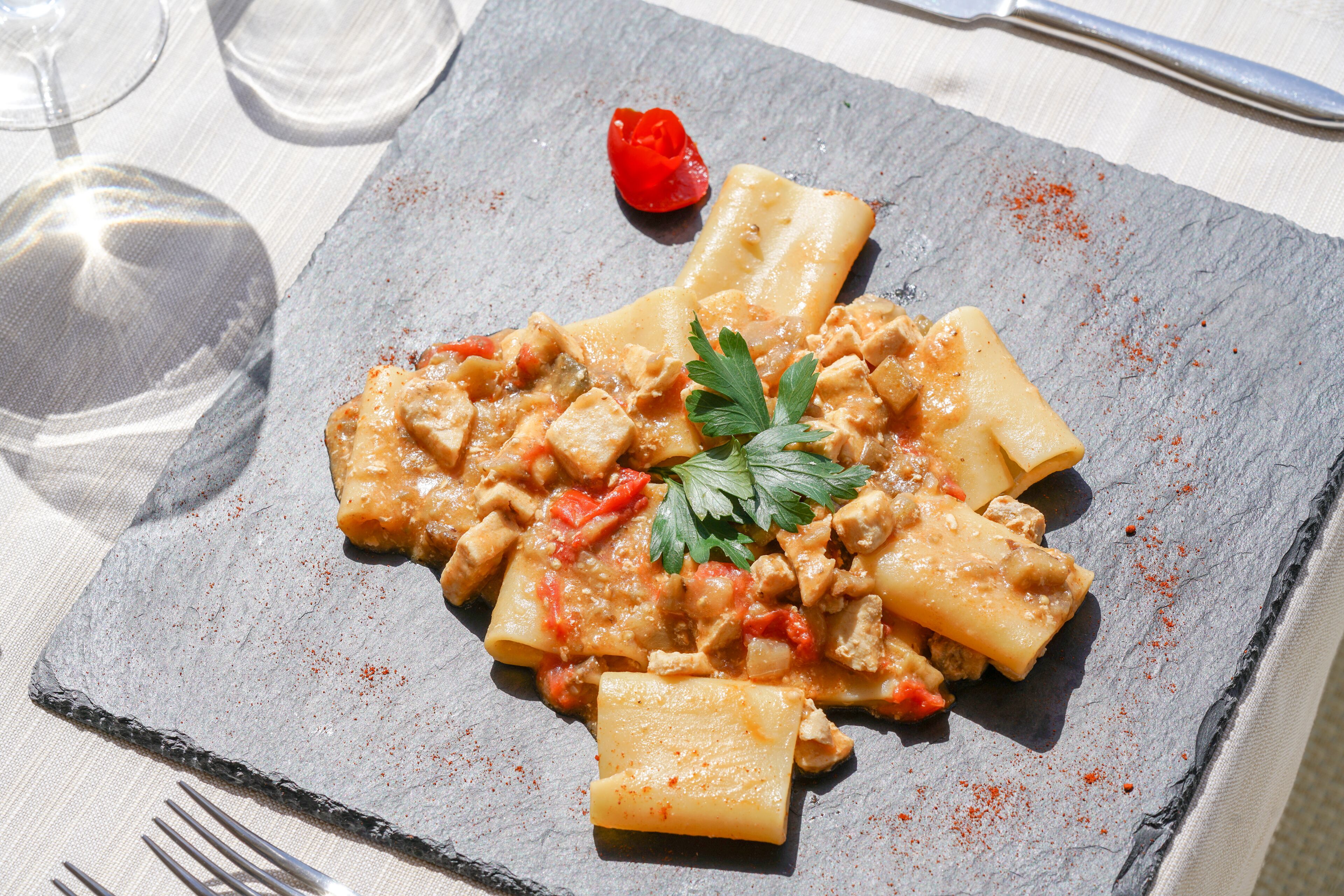A plate of pasta with a tomato-based sauce, garnished with parsley, on a slate serving board.