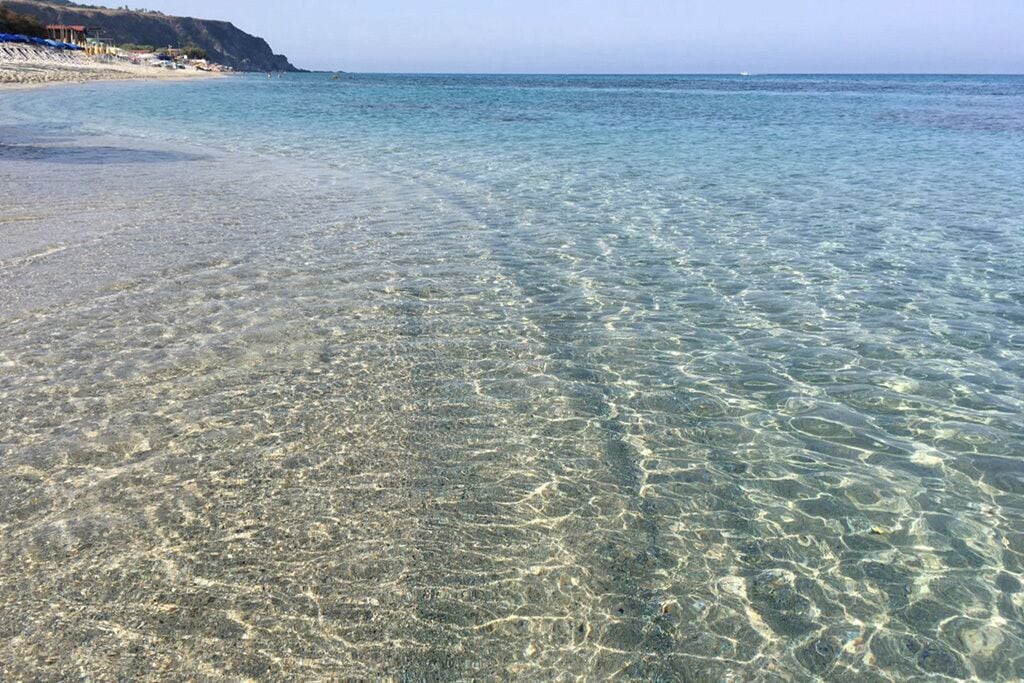 A beach with clear shallow waters and a sandy shore.