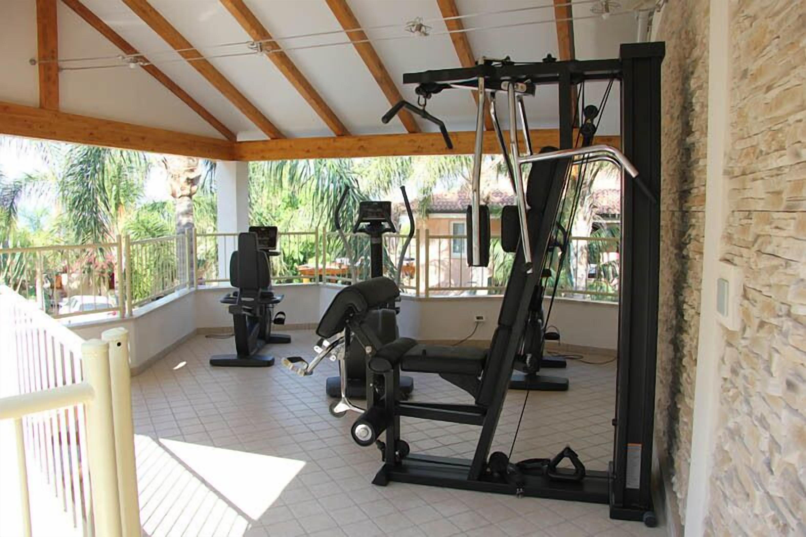 A covered outdoor gym with exercise equipment, a wooden ceiling, and a view of greenery.