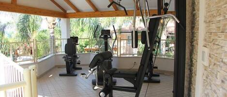 A covered outdoor gym with exercise equipment, a wooden ceiling, and a view of greenery.