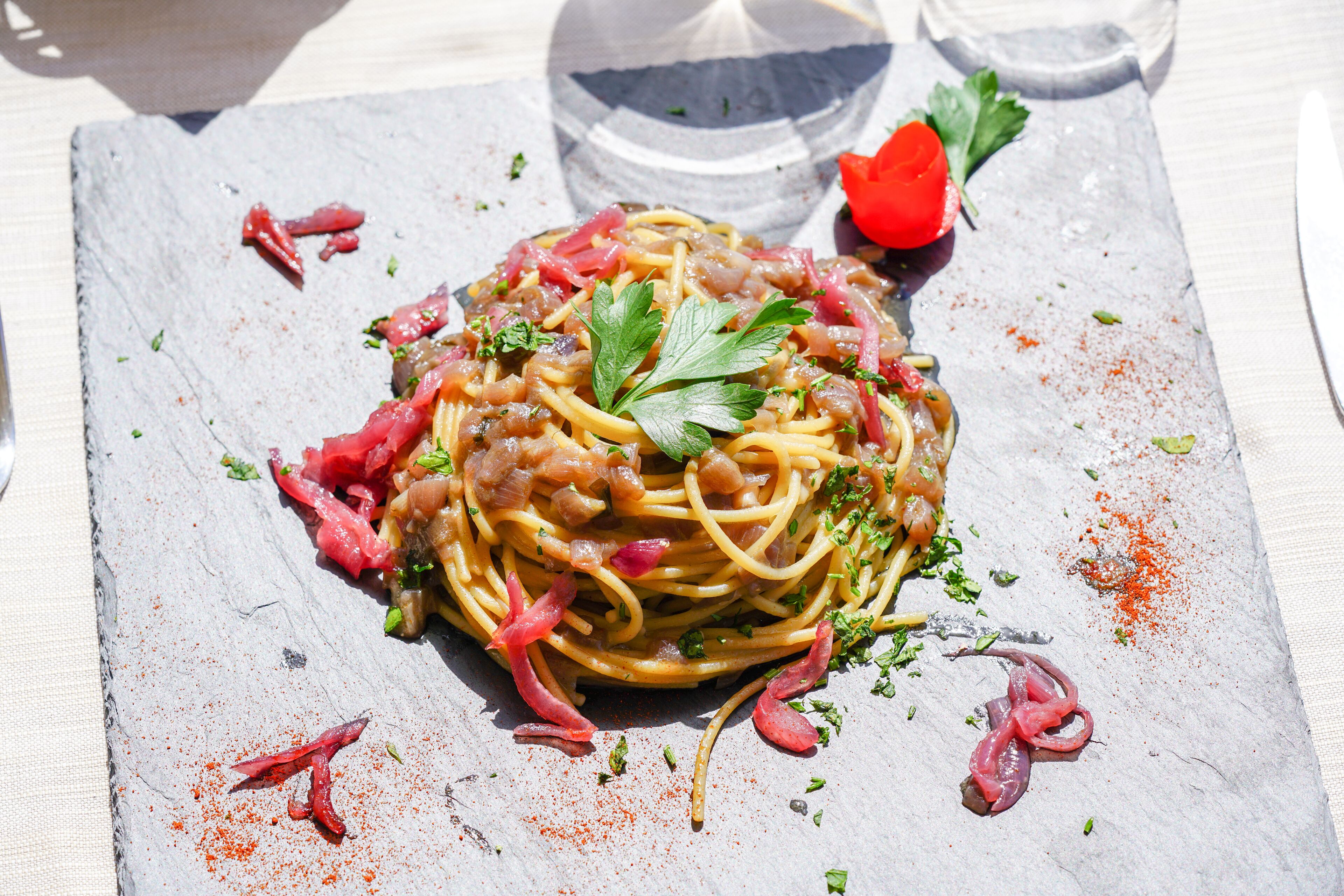 A plate of spaghetti with meat and vegetables, garnished with parsley, on a slate serving board.