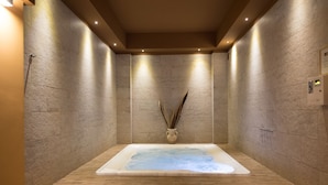 Un cuarto de spa con una bañera grande, paredes de piedra y piso de madera.