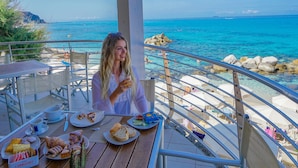 Una terraza con una mesa preparada para comer, con vistas a una zona costera con rocas y el mar.