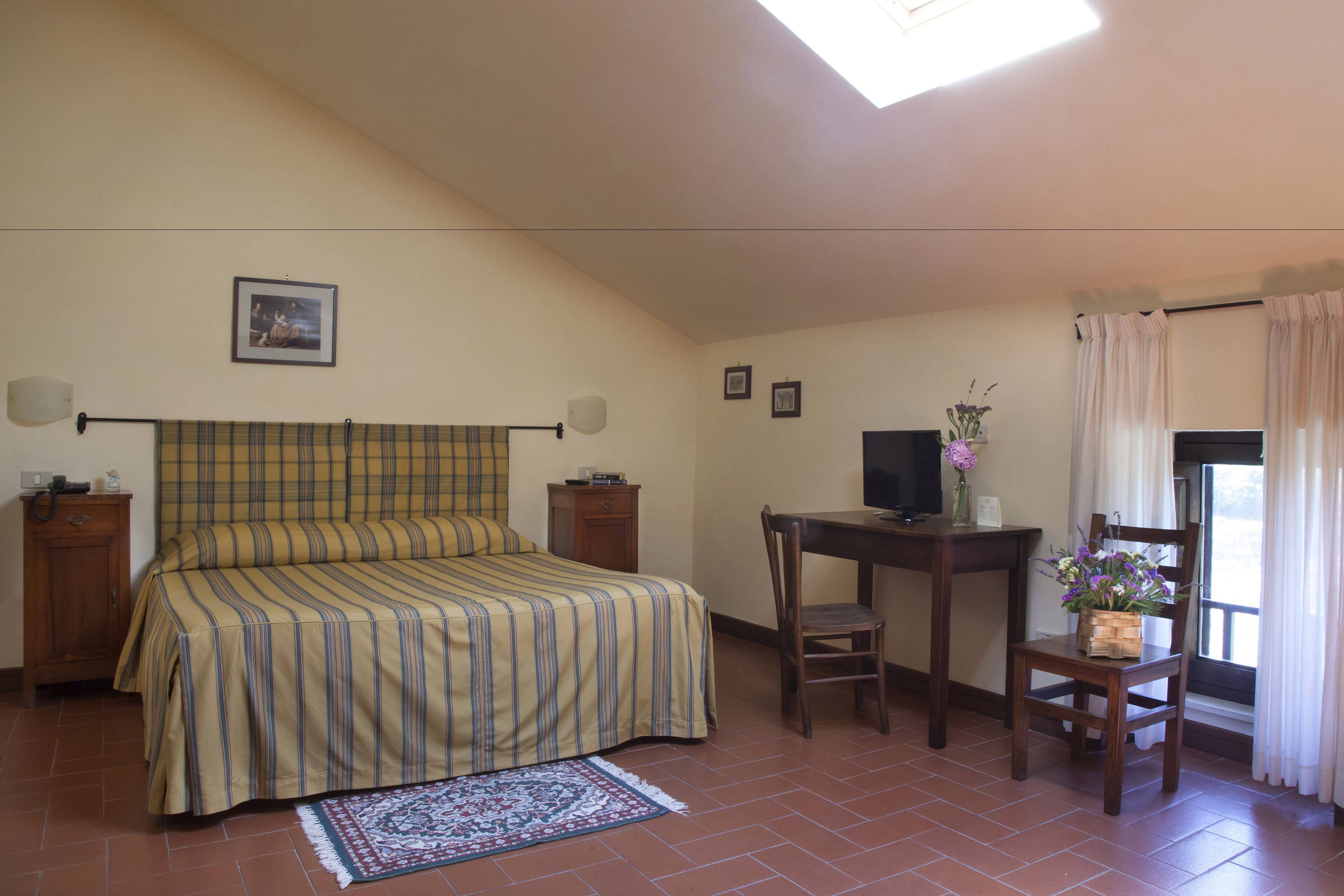 A bedroom with a bed, a desk, a chair, a TV, and a window with curtains.