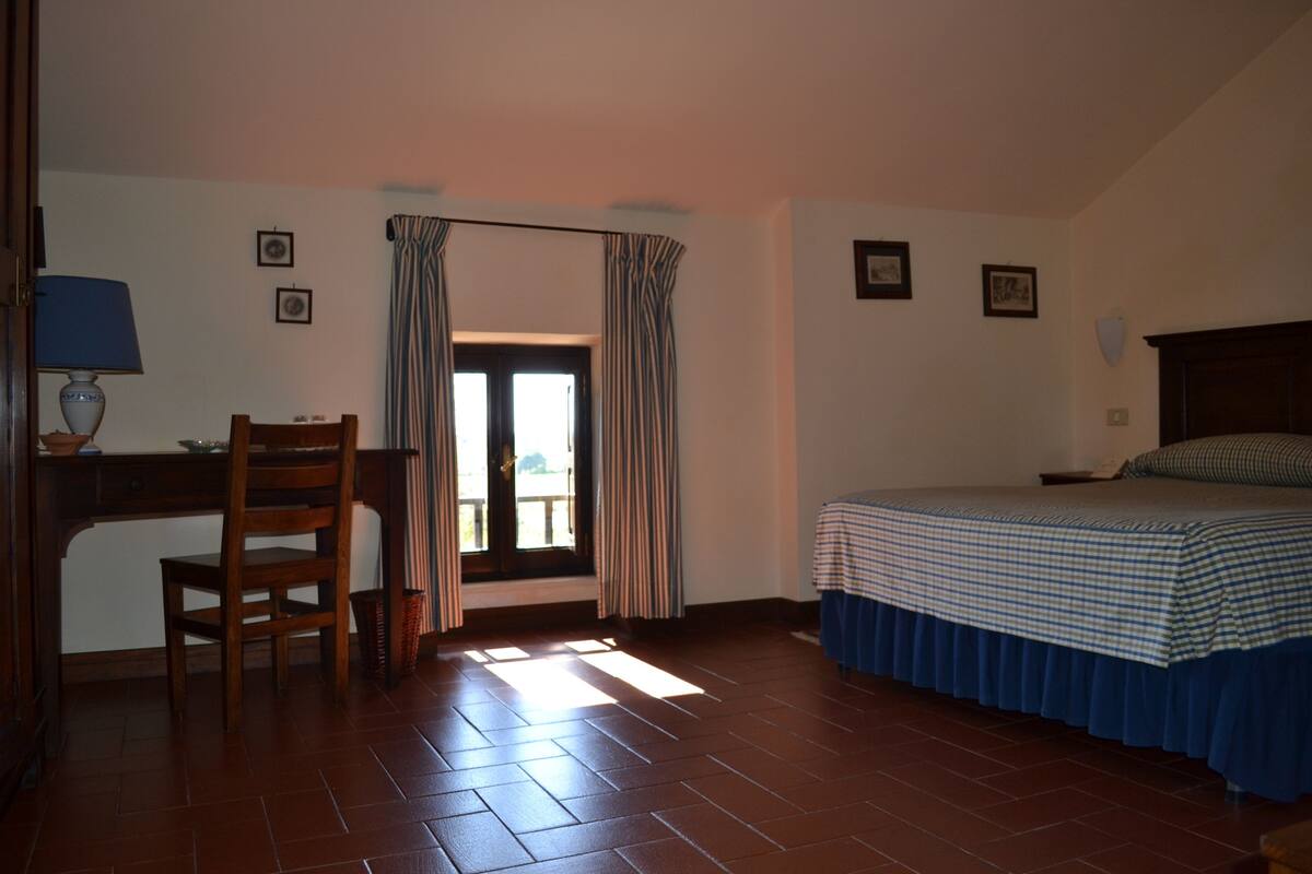 A bedroom with a bed, a desk, a chair, and a window with curtains.