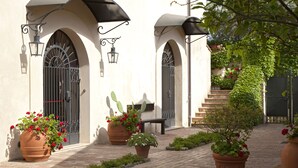 A courtyard with a tiled floor, two arched doorways with black metal grilles, a bench, and potted plants. - Il Granaio dei Casabella (Capaccio-Paestum)