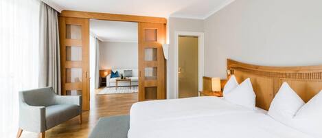 A hotel room with a large bed, a chair, a desk, and a view of the hallway.