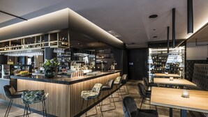 A modern bar area with a wooden counter, bar stools, and a seating area with a table and chairs. - Hotel Post (Brunico)