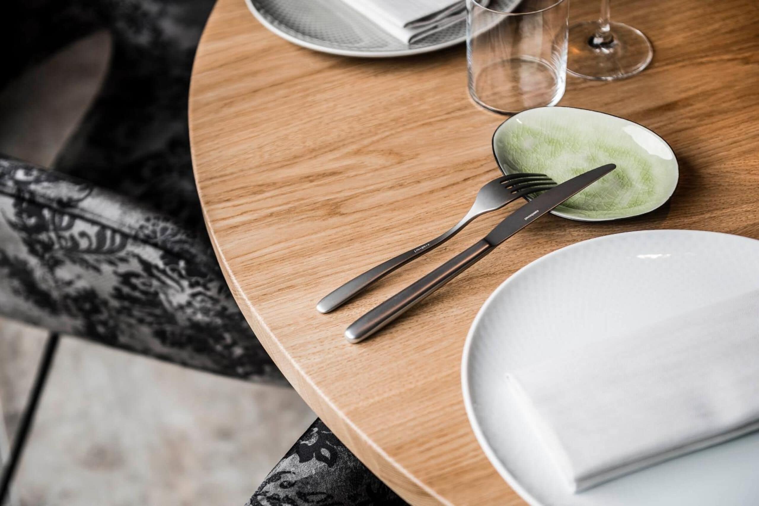 A neatly set dining table with a plate, fork, knife, and napkin, along with a glass of water and a menu.