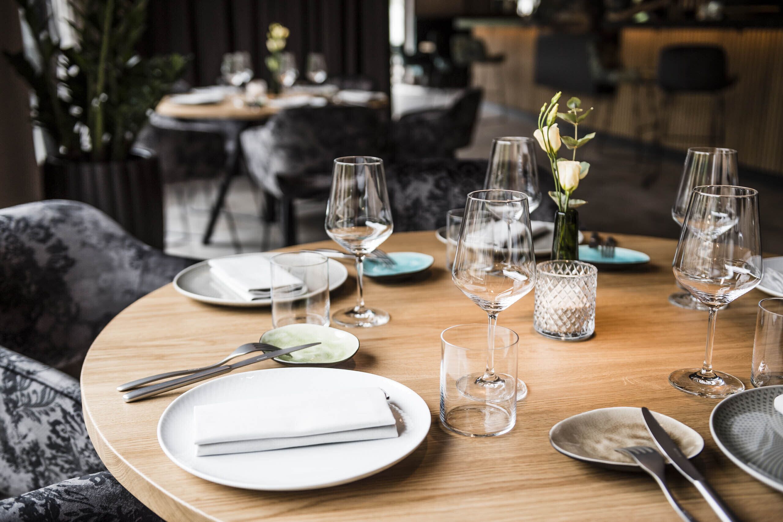 A dining table set with plates, cutlery, and wine glasses, with a vase of flowers and a decorative candle holder.