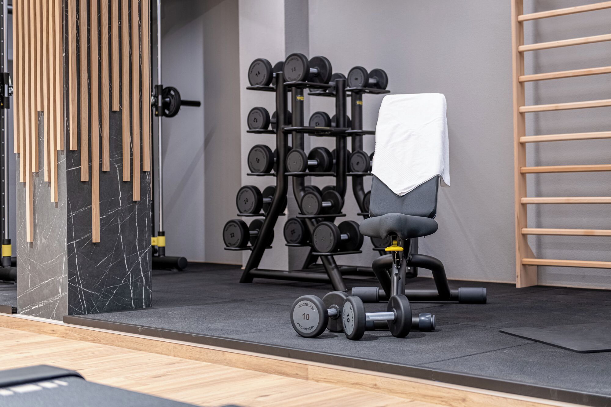 A gym with a rack of dumbbells, a bench, and a wooden wall.