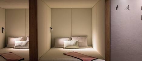 A room with two beds, each with pillows and a blanket, and a wooden panel on the wall.