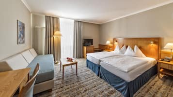 A hotel room with two beds, a sofa, a desk, a TV, and a lamp.