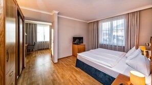 A hotel room with a large bed, a TV, a desk, and a view of the city through the window.