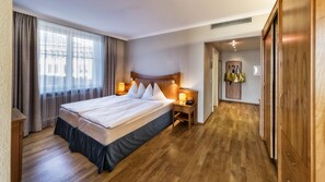 A hotel room with a large bed, wooden flooring, a nightstand with a lamp, and a wardrobe.