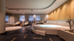 A modern spa area with a hot tub, lounge chairs, and a wooden wall. - Hotel Post (Brunico)