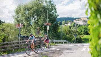Zwei Radfahrer auf einem befestigten Weg mit Hinweisschildern und einem Holzzaun.