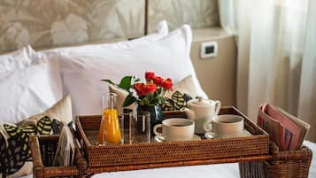 Una cama bien arreglada con una bandeja de desayuno que incluye zumo de naranja, tazas de café y una tetera.