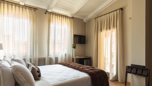 Une chambre d’hôtel avec un lit, des rideaux, une télévision, une petite table avec un vase et un plancher en bois.