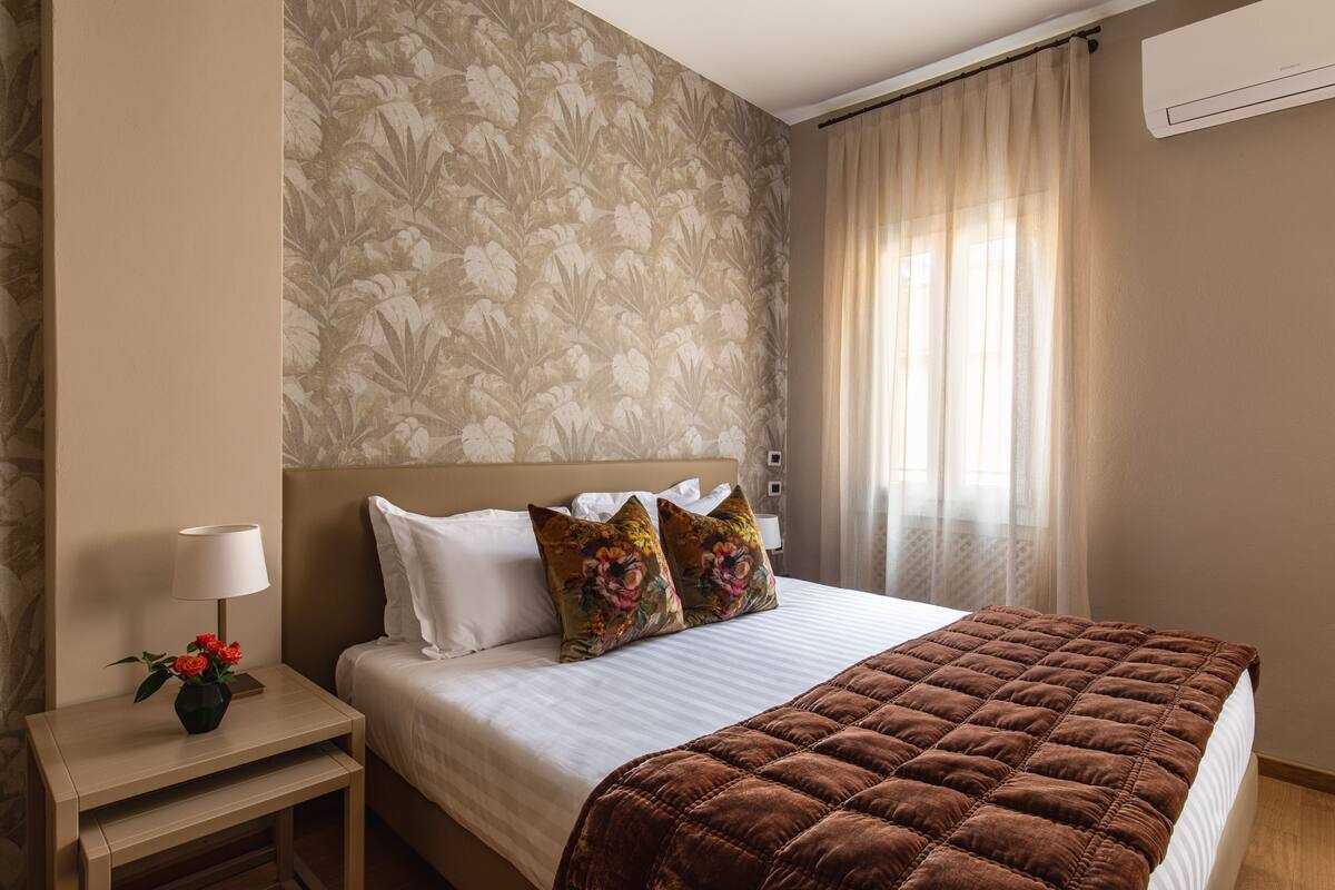 Une chambre d’hôtel avec un lit, une table de chevet avec une lampe et un papier peint à motifs floraux.