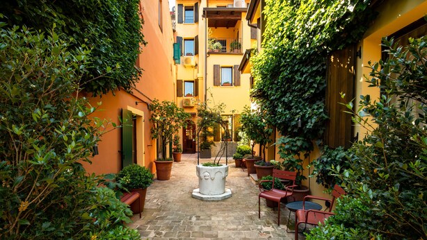 Une cour étroite avec une fontaine centrale, bordée de plantes en pot et dotée d’un espace pour s’asseoir à l’extérieur.