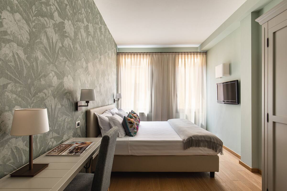 Une chambre d’hôtel équipée d’un lit, d’une table de chevet, d’une lampe et d’un téléviseur.