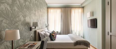 Quarto de hotel com cama, mesa de cabeceira, abajur e televisão.