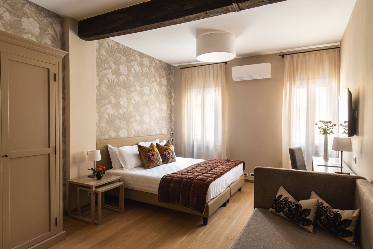 Une chambre à coucher avec un lit, des tables de chevet, un canapé, une télévision et une fenêtre avec des rideaux.