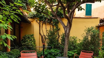 A courtyard with red metal chairs, a small table, and a tree providing shade.