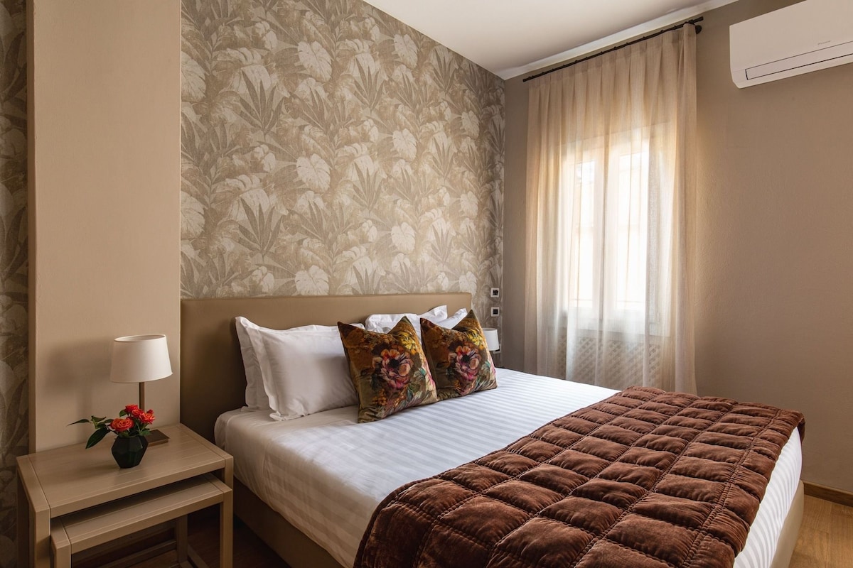 Een hotelkamer met een bed, een nachtkastje met een lamp en behang met bloemen.