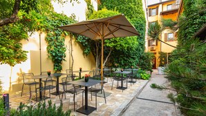 Une terrasse extérieure avec un sol en pierre, des tables et des chaises en métal, et un grand parasol.