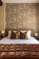 Una cama bien hecha con un edredón marrón, dos almohadas florales y un cabecero sobre un fondo de papel tapiz floral.
