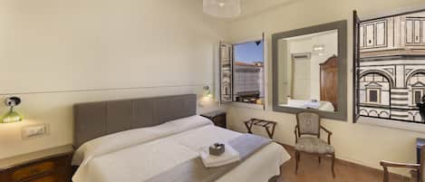 A bedroom with a bed, a chair, a desk, and a large mirror reflecting a building.