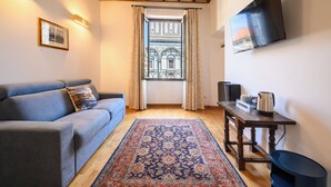 A living room with a blue sofa, a patterned rug, a wooden table with a kettle, and a TV on the wall. - Soggiorno Battistero (Florence)