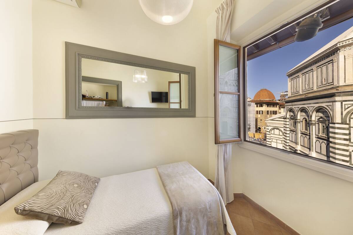 A bedroom with a bed, a large mirror, and a window with a view of a historic building.