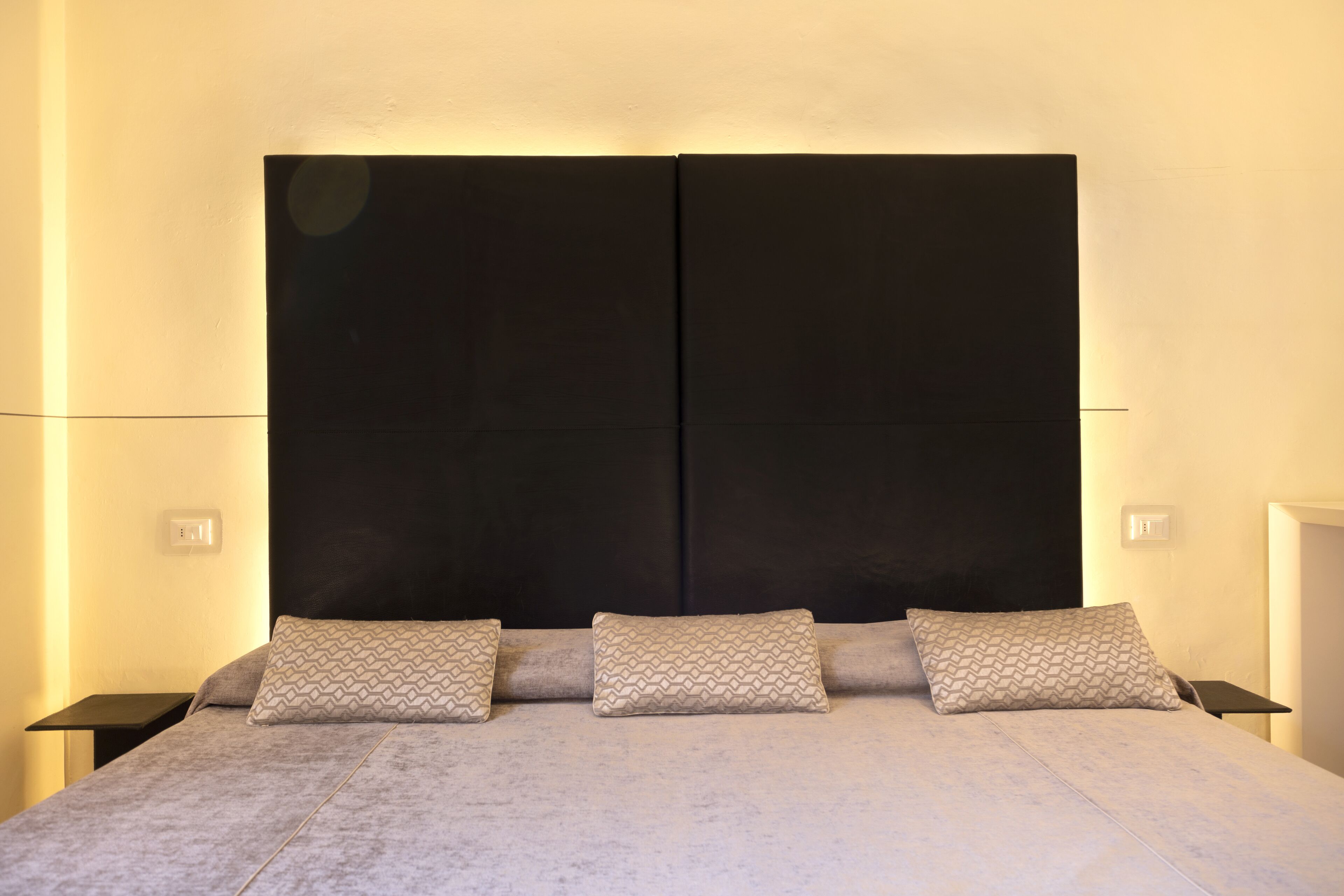 Un lit doté d’une grande tête de lit sombre, de trois coussins à motifs et d’une couvre-lit de couleur claire.