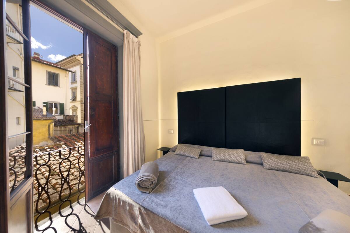 A hotel room with a large bed, a dark headboard, and a view of the outside balcony.