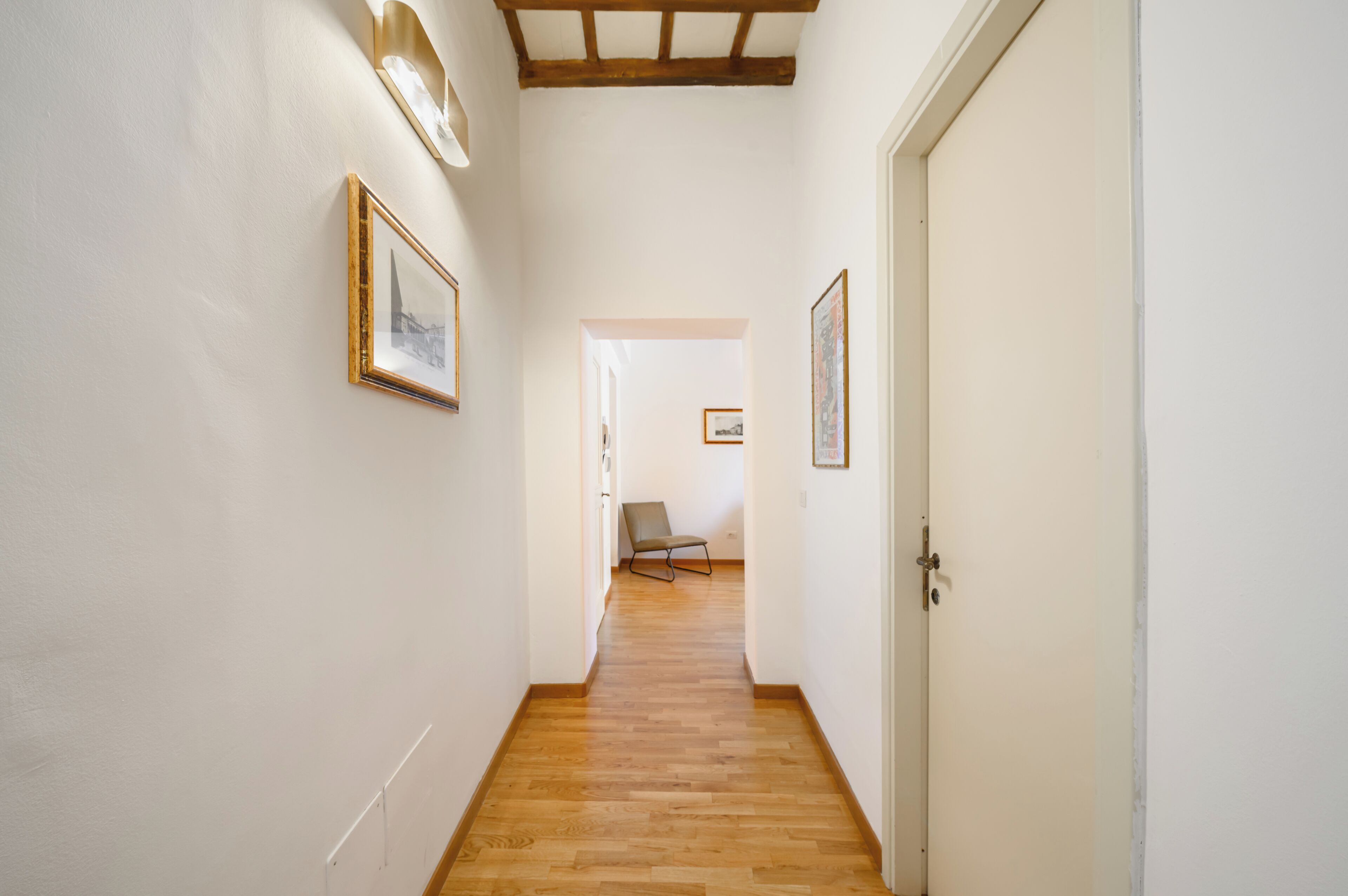 A hallway with wooden flooring, white walls, and framed pictures on the walls.