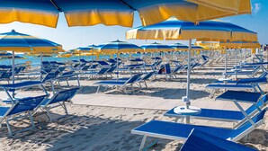Une plage bordée de rangées de parasols et de chaises longues aux rayures bleues et jaunes.
