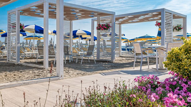 Une zone de plage agrémentée de pergolas blanches, de parasols bleus et jaunes, et de chaises longues blanches.
