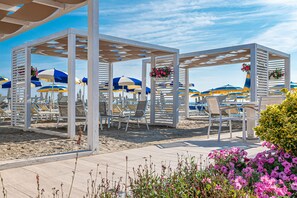 A beach area with white pergolas, blue and yellow umbrellas, and white lounge chairs. - Ausonia (Cervia)