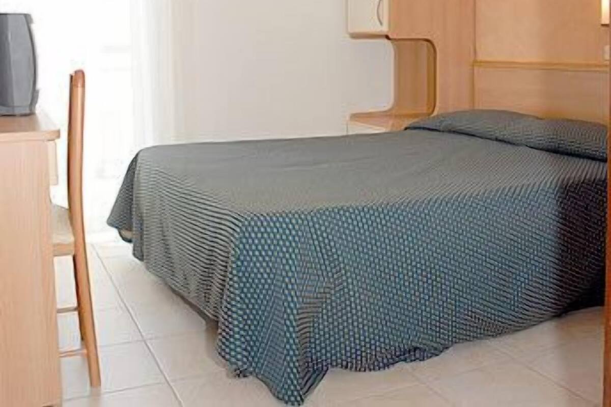 A neatly made bed with a patterned bedspread, a wooden nightstand with a television, and a chair.