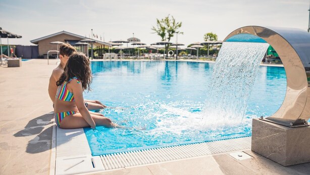 A swimming pool with a water feature, lounge chairs, and umbrellas. - Hotel Baya Strand (Cervia)