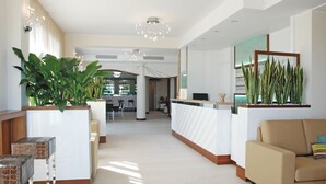 A modern hotel lobby with a reception desk, seating area, and a large plant. - Hotel Baya Strand (Cervia)