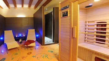 Un cuarto de spa con dos sillones de masaje, una mesita con velas y una zona de sauna de madera.