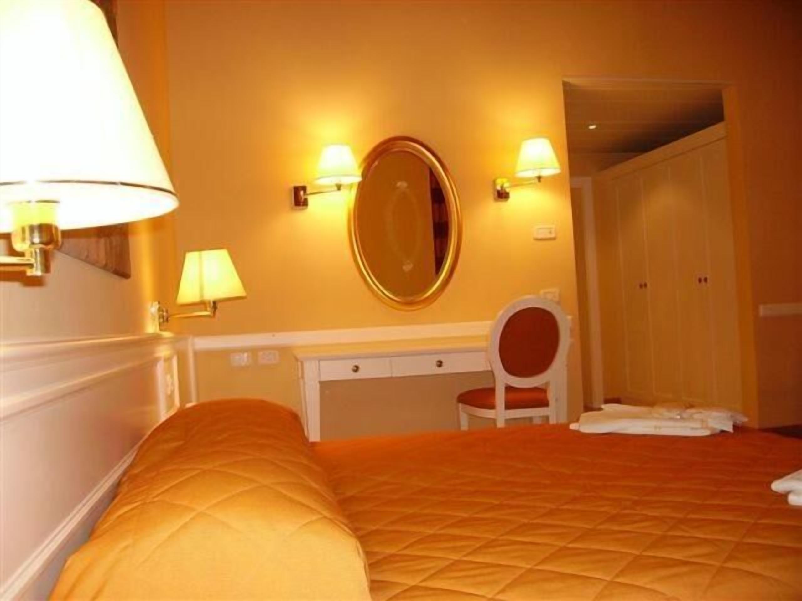 Una habitación de hotel con cama, escritorio, silla y espejo.