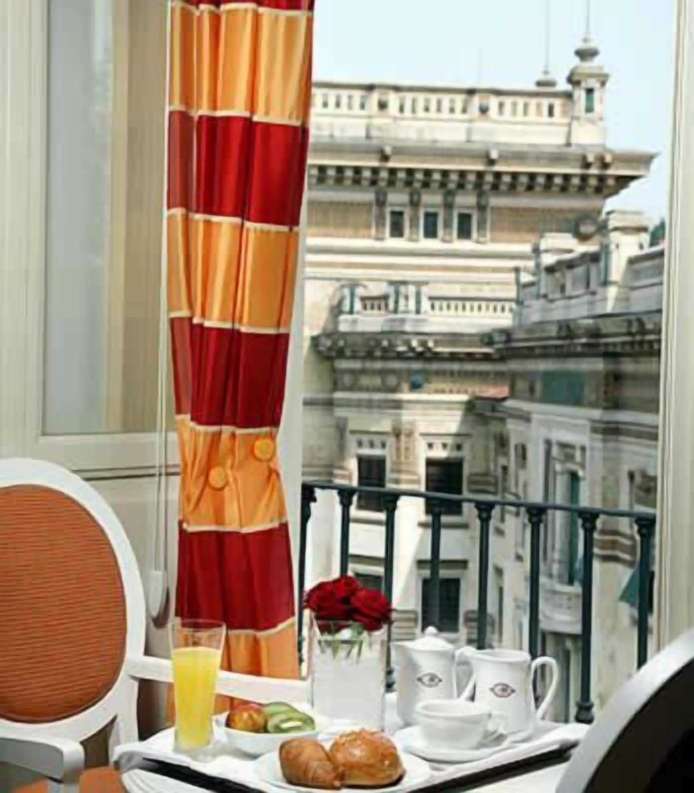 Un balcón con una mesa dispuesta para el desayuno, que incluye croissants, un vaso de zumo de naranja y tazas de té blancas.