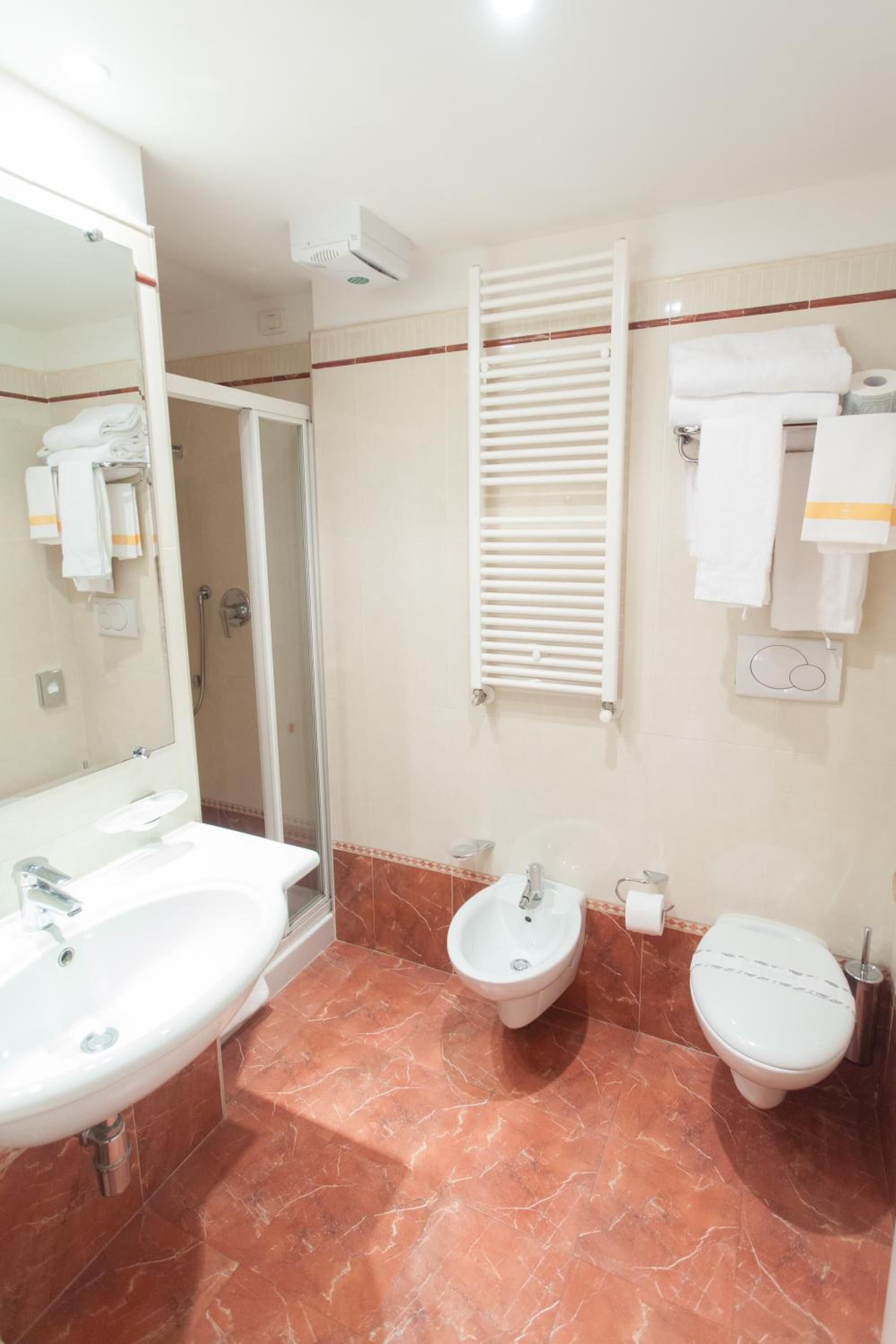 Un bagno con lavandino, bidet, WC, uno specchio, un portascopino e una zona doccia.